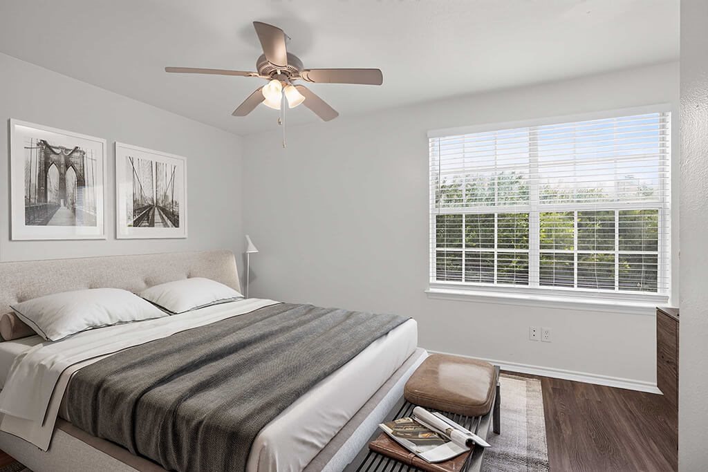A bedroom with a bed, a ceiling fan, and two framed pictures on the wall.